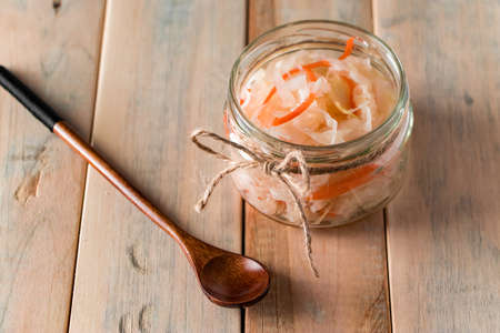 Homemade sauerkraut on a light wooden background. Glass jar with homemade fermented cabbage. Eco...