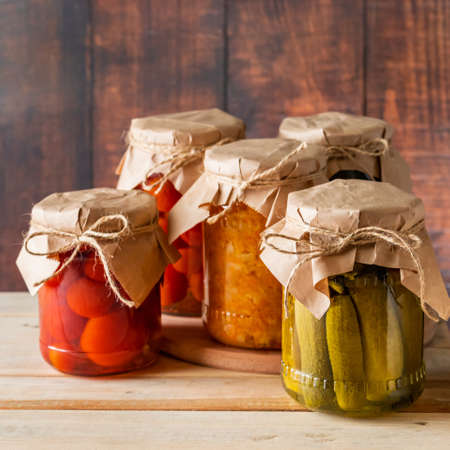 Pickled farm vegetables in glass jars on a wooden background. Fermented trending food. Home rustic style.の写真素材