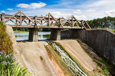 Old dam with a wooden bridge. View of the summer sunny landscape.