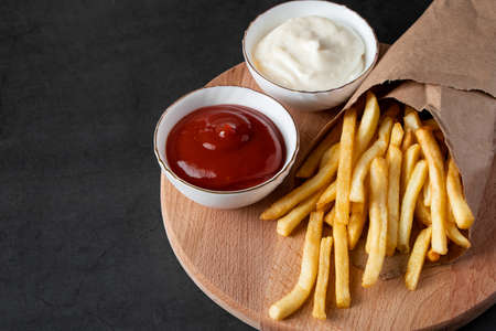Appetizing crispy fries in an eco-friendly paper bag on a black background. Hot american fast food.の写真素材