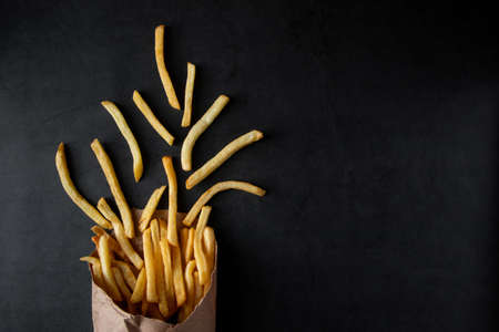 Hot crispy fries in a paper bag on a black background. Tasty american fast food. Place for textの写真素材