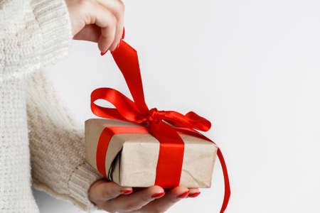 Gift with a red ribbon in hands on a white background. Woman unpacks a gift with a red ribbon on a white background.の写真素材