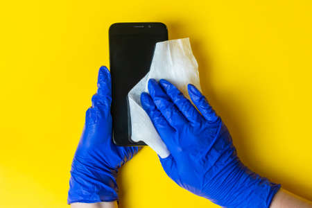 Hands in latex gloves disinfect the smartphone with an antiseptic. The concept of preventive...