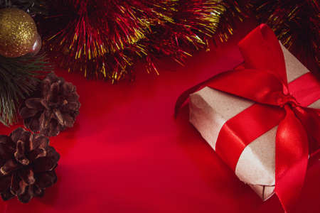 New Year's gift with a red ribbon in craft brown paper. Christmas composition of cones, tinsel and gifts on a red background.の写真素材