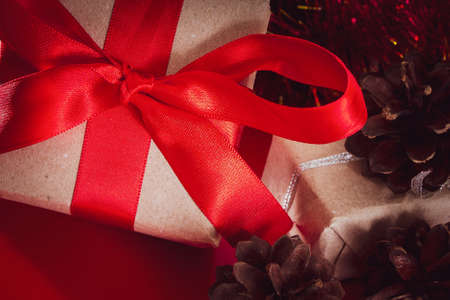 New Year's gift with a red ribbon in craft brown paper. Christmas composition of cones, tinsel and gifts on a red background.の写真素材