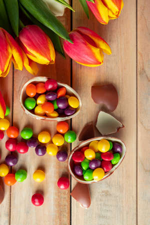 Bright multi-colored tulips and chocolate Easter eggs on a wooden background. Festive design, place for text, vertical photoの写真素材