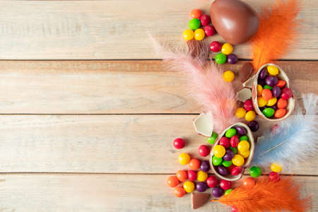 Composition of chocolate Easter eggs and delicate feathers on a light background. Multi-colored...