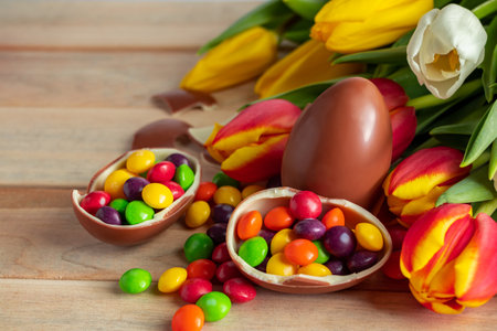 Beautiful red and yellow tulips for easter holiday. Chocolate eggs and candies on a wooden...