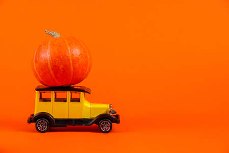 Retro toy car with a pumpkin on an orange background. Halloween and autumn harvest concept, place for text.の写真素材