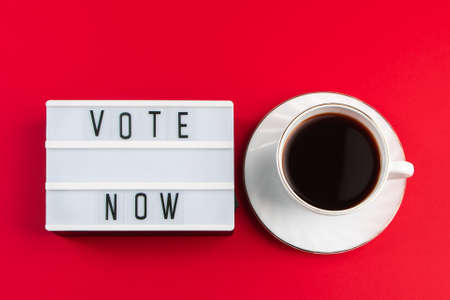 Vote now. Sign and cup of coffee on a red background. Election voting concept.の写真素材