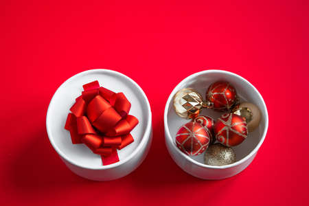 Open gift box with Christmas balls on a red background.