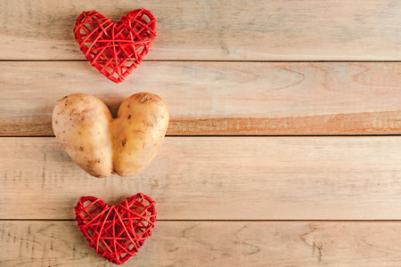 Heart shaped potato on wooden background. Valentines day, place for text. Ugly vegetables.の写真素材