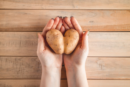 Heart shaped potatoes in hands on wooden background. Valentine's day concept. Ugly vegetables.の写真素材