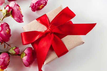 Gift box with red ribbon and delicate pink flowers on white background. Surprise on Womens Day and...