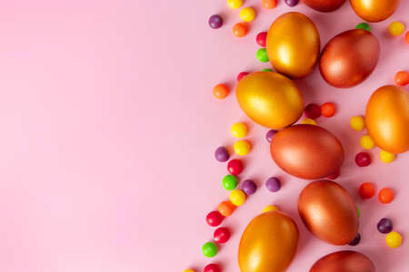 Golden Easter eggs and candies on a pink background. Happy spring holiday, place for text.