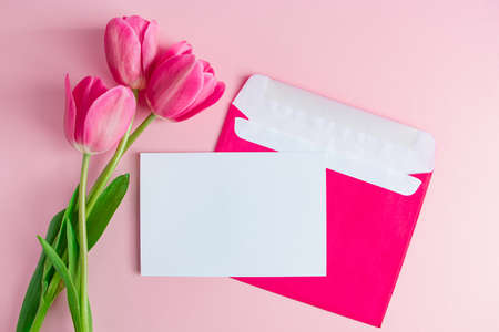Envelope with invitation to holiday and  bouquet of tulips on pink background. Place for text.