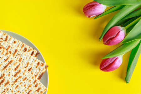 Traditional Jewish food matzo bread and pink tulips on yellow background. Happy Passover. Religious spring holiday Pesach. Copy space.の写真素材