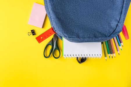 School backpack with office supplies on a yellow background. Place for text.の写真素材
