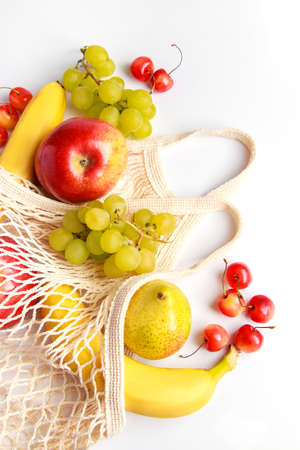 Organic ripe fruits in eco-friendly mesh bag on a white background. Trendy string bag for shopping. Healthy eating and sustainable lifestyle concept. Zero waste.の写真素材
