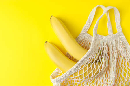 Ripe bananas in a mesh bag on a yellow background. Eco-friendly cotton shopping bag. Organic fruits. Sustainable lifestyle and recyclable waste concept.の写真素材