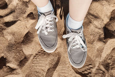 Legs in gray sneakers on the beach sand. Summer vacation concept by the sea. Lifestyle travel. Pov...