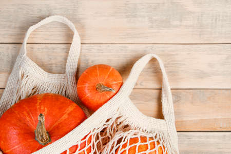 Ripe pumpkins in mesh bag on a wooden background. Eco-friendly farm products. Autumn harvest and Thanksgiving concept. Copy space.の写真素材