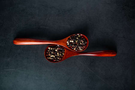 Wooden spoon with mix of pepper on a black background. Dried aromatic spice.の写真素材