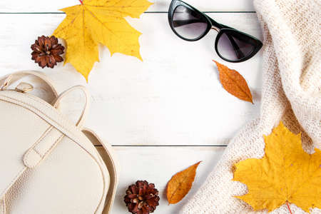 Hello autumn. Creative flat lay composition on white background. Yellow leaves, knitted sweater, backpack and glasses. Copy space.の写真素材