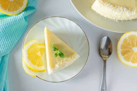 Piece of biscuit dessert with lemon and coconut flakes. Layered vanilla cake on a white plate.の写真素材