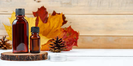 Essential oil bottle for aromatherapy. Autumn skin care concept. Cosmetic serum on a wooden pedestal. Eco-friendly trendy cosmetics. Copy space.の写真素材