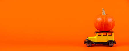 Retro toy car with a pumpkin on an orange background. Halloween and autumn harvest concept, place for text.の写真素材