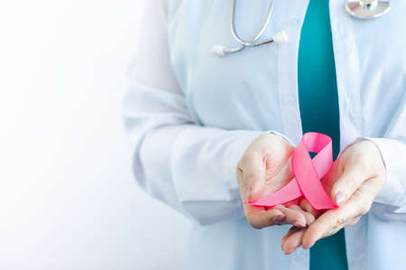 Breast Cancer Awareness Month. Female doctor in medical white uniform holds pink ribbon in her hands. Womens health care concept. Copy space.の写真素材