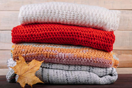 Stack of warm knitted sweaters. Autumn concept. Woolen jumpers and maple leaf on a wooden background.の写真素材