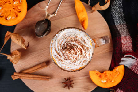 Pumpkin coffee latte with whipped cream on dark background. Hot autumn drink with cinnamon and spices in glass mug on wooden tray. Fall and coziness concept.の写真素材