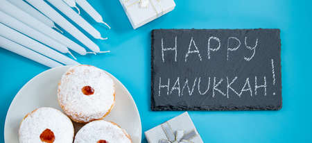 Happy Hanukkah. Jewish dessert sufganiyot donuts on blue background. Symbol of religious Judaism holiday. Inscription on the chalk board.の写真素材