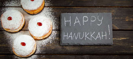 Happy Hanukkah. Traditional dessert Sufganiyot on dark wooden background. Donuts, candles and gifts. Celebrating Jewish religious holiday. Banner format.の写真素材