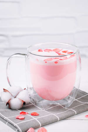 Pink matcha with rose petals on a white background. Transparent cup with trendy vegan whipped tea....