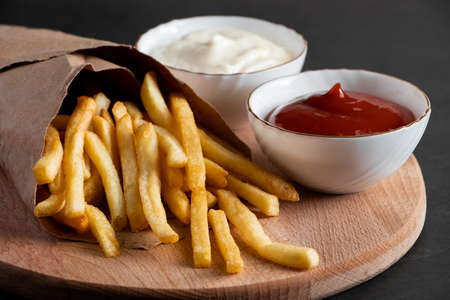 Hot crispy fries in a paper bag on a black background. Tasty american fast food.の写真素材