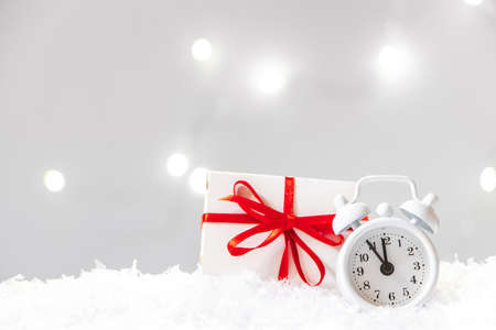 Gift box and alarm clock in snow on bokeh background. New Year concept, place for text.