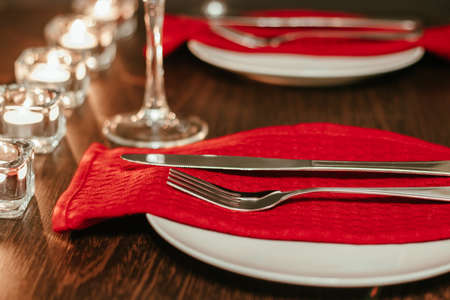 Christmas table setting. Plate and cutlery on a napkin. Preparing for festive dinner. Candles burning on table on Christmas Eve.の写真素材
