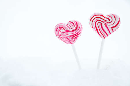 Two pink heart-shaped lollipop. Caramel candy on a stick on white background. Sweet gift for...