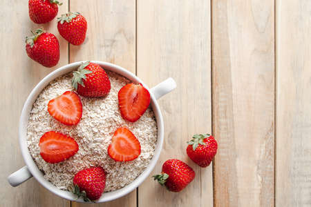 Oat flakes with strawberries in bowl on wooden background. Healthy breakfast. Concept of diet and gluten-free cereals. Copy spaceの写真素材