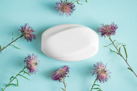 White cosmetic soap and dry flowers on blue background. Hygiene and skin care. Natural herbal...