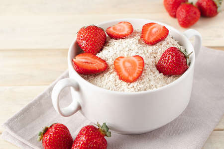 Oat muesli and fresh strawberries on wooden background. Healthy breakfast food. Bowl of oatmeal and berries on linen napkin. Concept of diet and gluten-free cereals.の写真素材