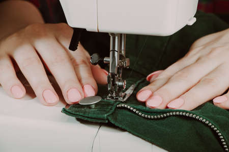 Woman designer or tailor working on sewing machine. Hands hold and sew on details of clothing. World tailors day. Close-up of sewing process.の写真素材