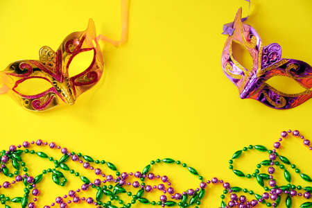 Two multi-colored carnival masks and beads on yellow background. Mardi Gras concept. Fat Tuesday symbol. Festive decorations close-up. Copy space.の写真素材