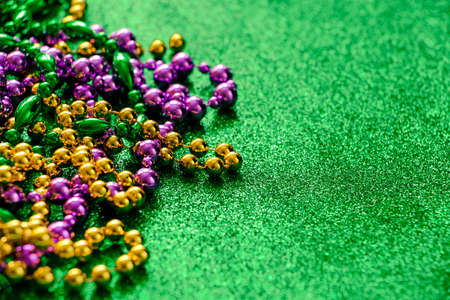Mardi Gras concept. Multi-colored beads on green shiny background. Fat Tuesday symbol. Festive shining decorations in gold, green and purple colors for traditional holiday. Copy space.の写真素材
