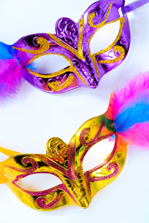 Two carnival masks with feathers and multi-colored beads on white background. Mardi Gras or Fat Tuesday symbol. Greeting card for for traditional holiday. Vertical photo.の写真素材