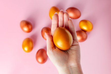 Woman holds shiny Easter golden egg in her hand. Festive decor on pink background.の写真素材