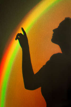 Shadow of woman. Rainbow reflection of sunbeam on wall. Hand touches rainbow beam. Concept of dreams...